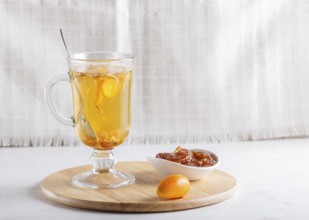 Jasmine tea with kumquat in a glass cup on a wooden board on a white background. close up, copy