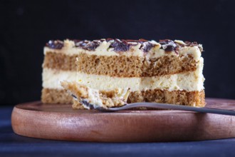 A piece of cake with milk and butter cream cutted with spoon on a wooden kitchen board, close up,