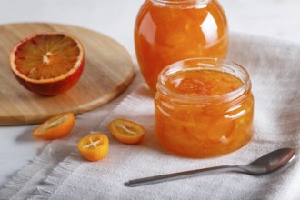 Orange and kumquat jam in a glass jar with fresh fruits on a white linen tablecloth. Homemade,