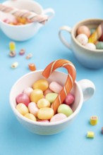 Heap of multicolored caramel candies in cups on blue pastel background. close up, side view,