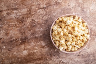 Popcorn with caramel in ceramic bowl on brown concrete background. Top view, flat lay, copy space