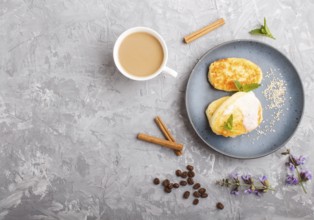 Cheese pancakes on a blue ceramic plate and a cup of coffee on a gray concrete background. top