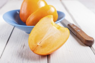 Ripe orange persimmon in a blue plate on white wooden background, with copy space