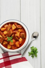 Potatoes stewed with meat, in tomato sauce, with spices and herbs, no people, on a white table