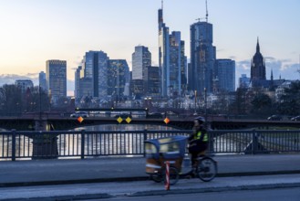 Skyline of the city centre of Frankfurt am Main, cargo bike cyclist on the rafter bridge, dusk,