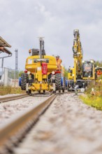 Yellow construction machinery working on a railway line under a cloudy sky, track construction