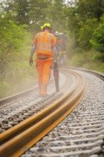 Construction worker in protective clothing walking next to railway tracks in the fog, track