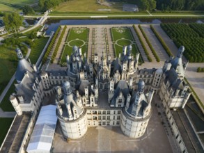 Detailed view of a historic castle from the air, with many towers and green areas all around,