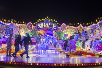 An illuminated carousel in the amusement park at night, people and shining lights, Cannstatter