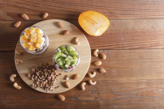 Dessert with greek yogurt, granola, almond, cashew, kiwi and persimmon on brown wooden background.