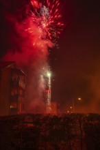 Fireworks explode at night over a residential building with smoke billowing in the background,