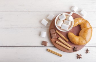 A cup of hot chocolate with marshmallow, croissant and spices on white wooden background. top view,