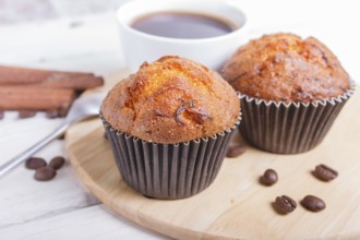 Two carrot muffins with cup of coffee on wooden kitchen board on white wooden background with