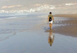 Man walking barefoot on sandy beach at low tide near village of Taghazout, Morocco, North Africa,