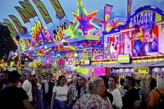 Lots of people in front of kitschy brightly coloured neon signs in the evening, Cranger Kirmes,