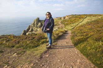 Woman wearing kagoule walking along the South West coast path at St Agnes head, Cornwall, England,