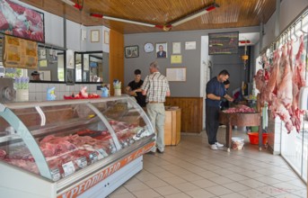 Customers and butchers in a butcher's shop full of meat products and a busy atmosphere, Gastouni,