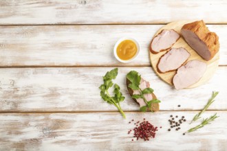 Smoked pork ham on cutting board with pepper and herbs on white wooden background. Top view, flat