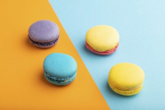 Yellow, purple and blue macaroons on blue and orange pastel background. side view, close up.