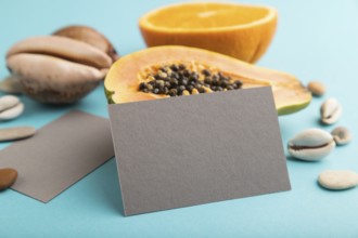 Gray paper business card with ripe cut papaya, orange, seashells on blue pastel pastel background.