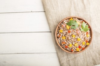 Buckwheat porridge with vegetables in wooden bowl on a white wooden background and linen textile.