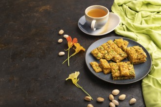 Traditional iranian dessert sohan with cup of green tea on a black concrete background and green