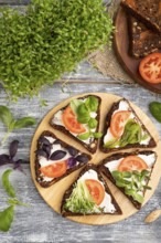 Grain rye bread sandwiches with cream cheese, tomatoes and cilantro microgreen on gray wooden