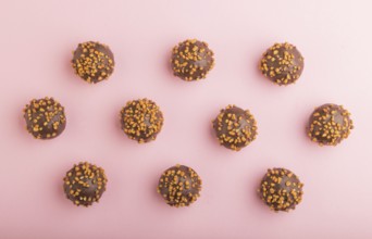 Chocolate caramel ball candies with almonds in a row on a pastel pink background. top view, flat