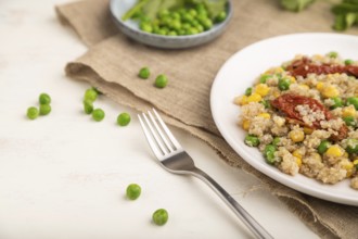 Quinoa porridge with green pea, corn and dried tomatoes on ceramic plate on a white wooden