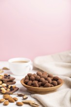 Almond in chocolate dragees in wooden plate and a cup of coffee on white and pink background and