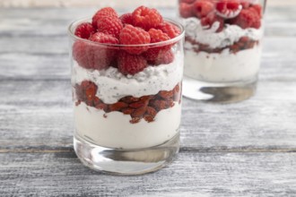 Yogurt with raspberry, goji berries and chia seeds in glass on gray wooden background. Side view,