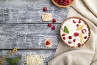 Rice flakes porridge with milk and strawberry in wooden bowl on gray wooden background and linen