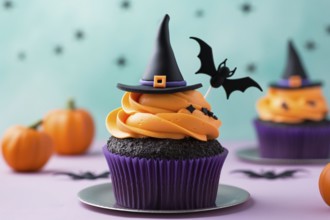 Black and purple Halloween cupcake with orange frosting, witch hat and bat decoration. KI