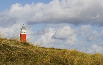 A red lighthouse stands on a grassy hill under a dramatic cloudy sky, Eierland lighthouse, Texel