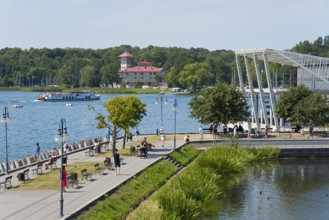 A lively lakeside promenade with a view of the lake, boats and an architectural bridge in the