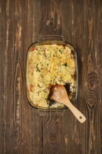 A casserole filled with cannelloni pasta, vegetables and herbs in a glass dish. A wooden spatula