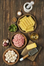 A variety of fresh ingredients is arranged on a wooden surface, featuring ground meat, pasta