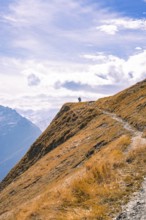 A stony path stretches over a mountain ridge with a lone hiker at the top, Planplatten,