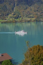 A ship cruises across the lake, against a background of forested mountains in autumn colours, Lake