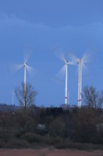 Luminous wind turbines rotating in an area surrounded by trees in the evening light, Wind turbines