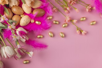 Arrangement in pink and gold made of flowers, feathers and Easter eggs on a pink background