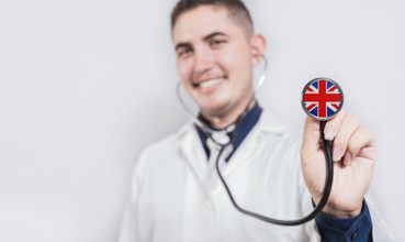 UK National Healthcare concept. Smiling doctor showing stethoscope with UK flag