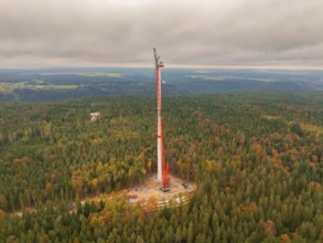 A tall crane installs a wind turbine in the middle of a colourful forest, wind farm construction