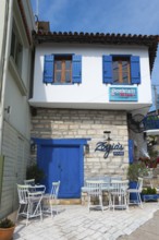 Mediterranean house façade with blue accents and terrace with white furniture under a slightly