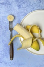 Opened banana on plate and fork with banana slice