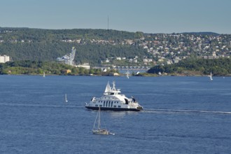 A ferryboat in the calm sea, with an urban landscape and green hills in the background, electric