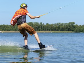 Young casual man with flapping shirt on wakeboard in lake, water ski and wakepark, Stráž pod