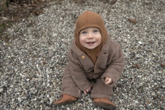 Laughing child, 8 months, wrapped up warm, sitting on the gravel and playing with stones,