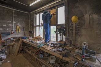 Young man in his workshop, standing on the workbench and repairing a window,