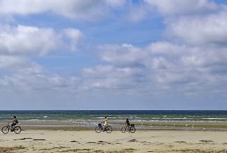 People riding bicycles along the beach, the sea and the sky with clouds in the background,